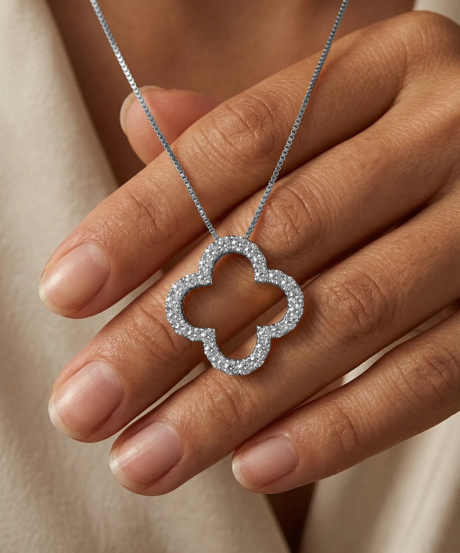 Silver quatrefoil pendant necklace held by a hand against a neutral background