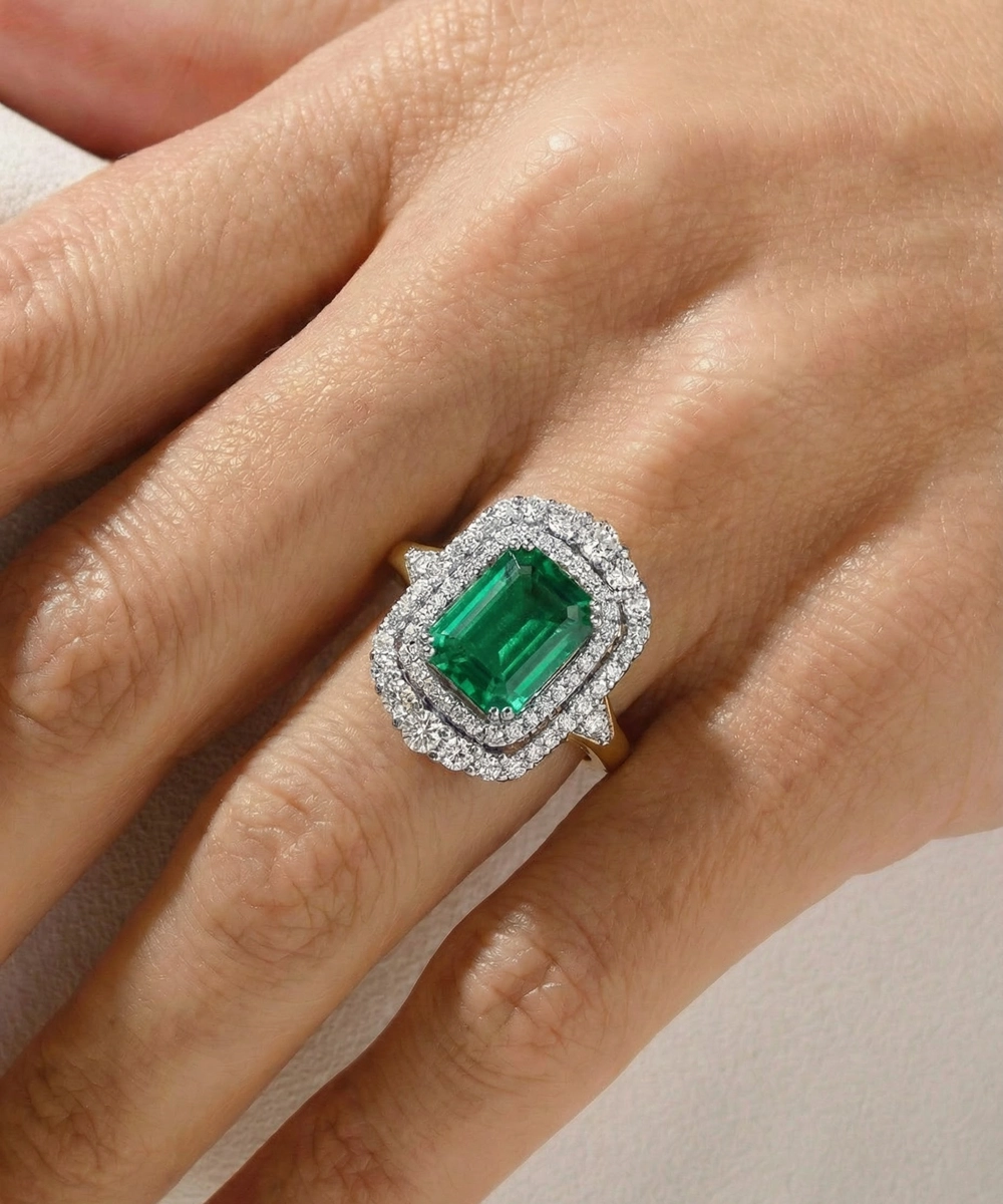 Emerald ring with diamond halo on a hand against a neutral background