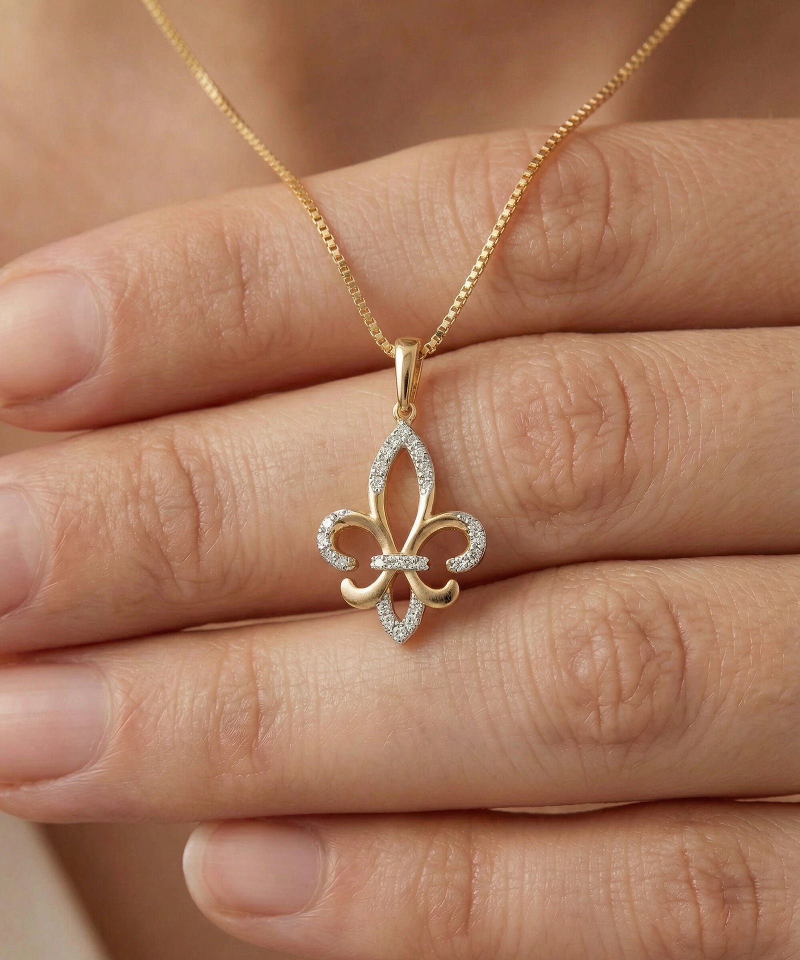 Gold and diamond fleur-de-lis necklace on a hand