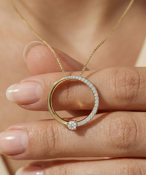 Gold necklace with a circular pendant held by a hand against a neutral background