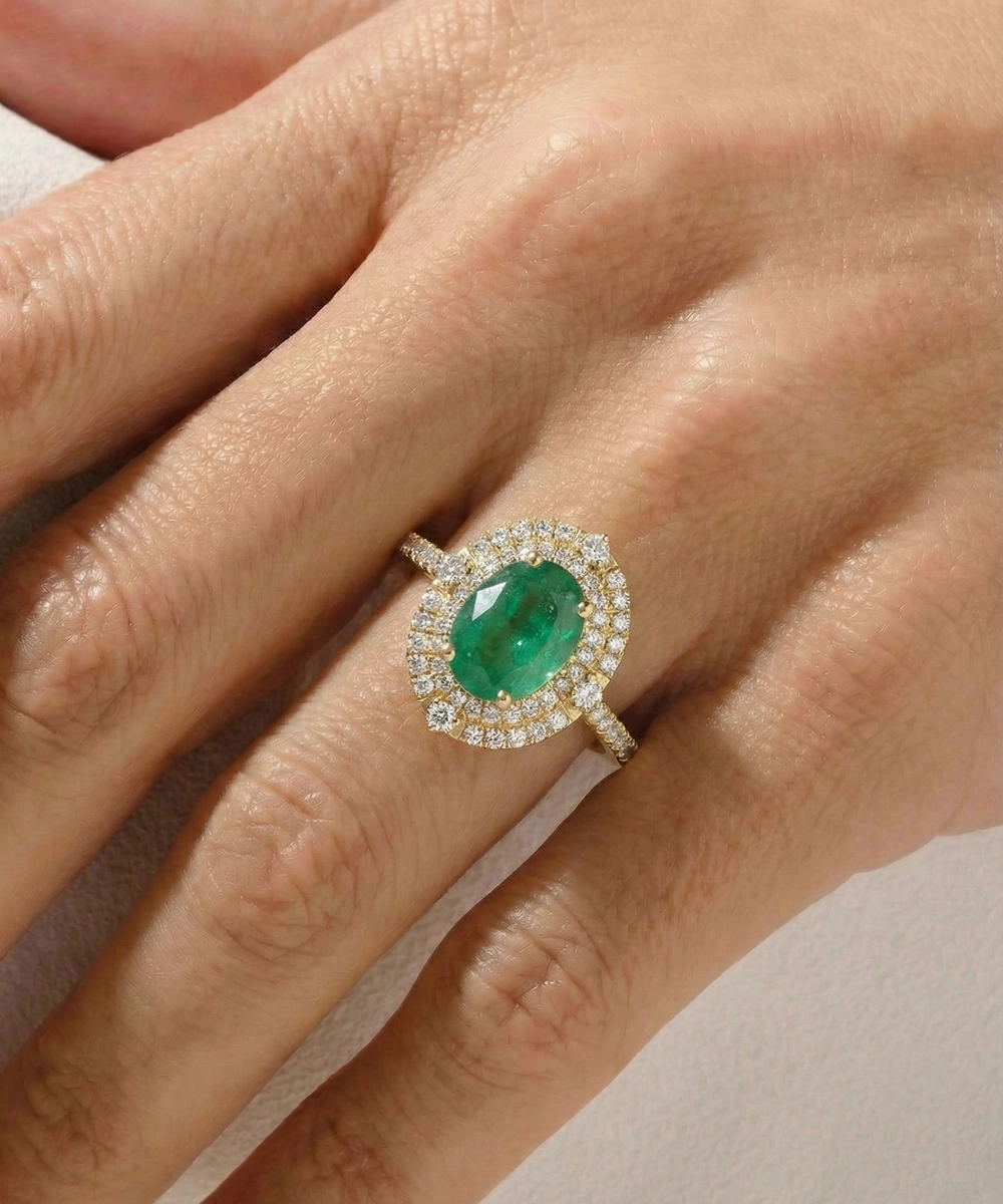 Emerald ring with diamond halo on a hand against a neutral background