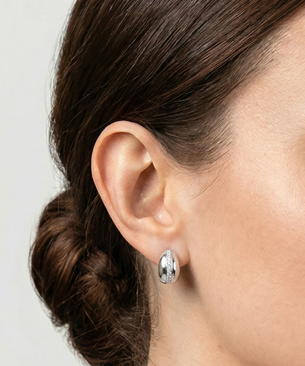 Close-up of an ear wearing a silver hoop earring with a plain background
