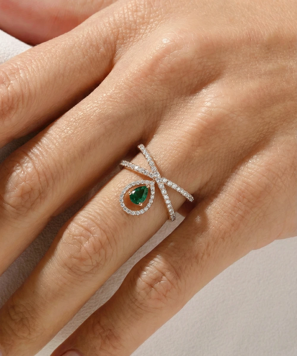 Silver ring with a green gemstone on a hand against a neutral background