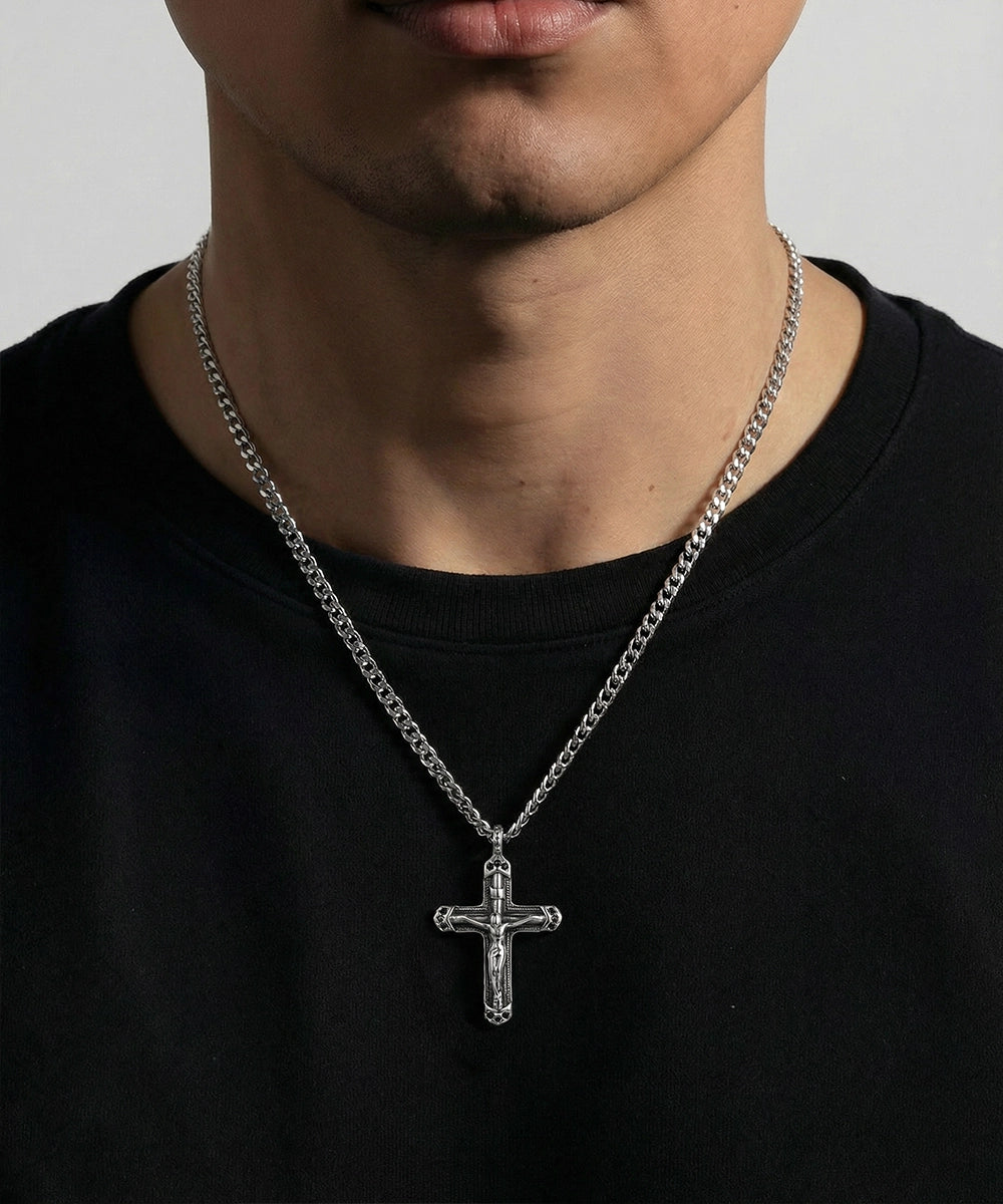Person wearing a black shirt with a silver chain necklace featuring a cross pendant.
