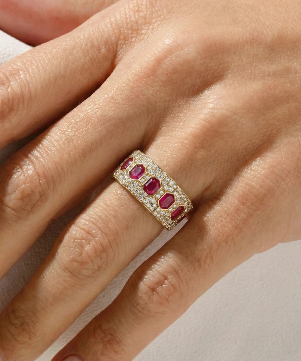Gold ring with red gemstones on a hand against a neutral background