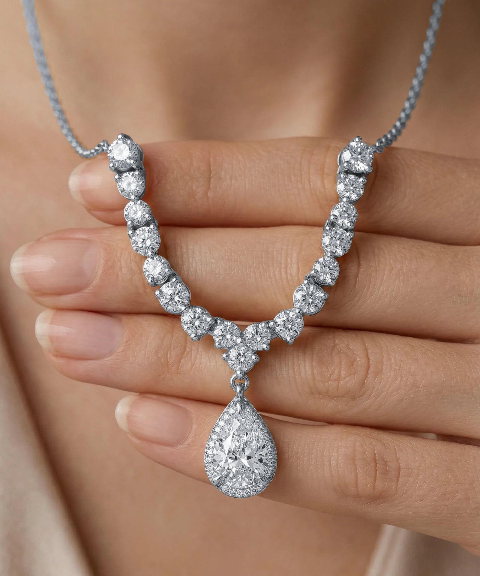 Diamond necklace held by a hand against a neutral background
