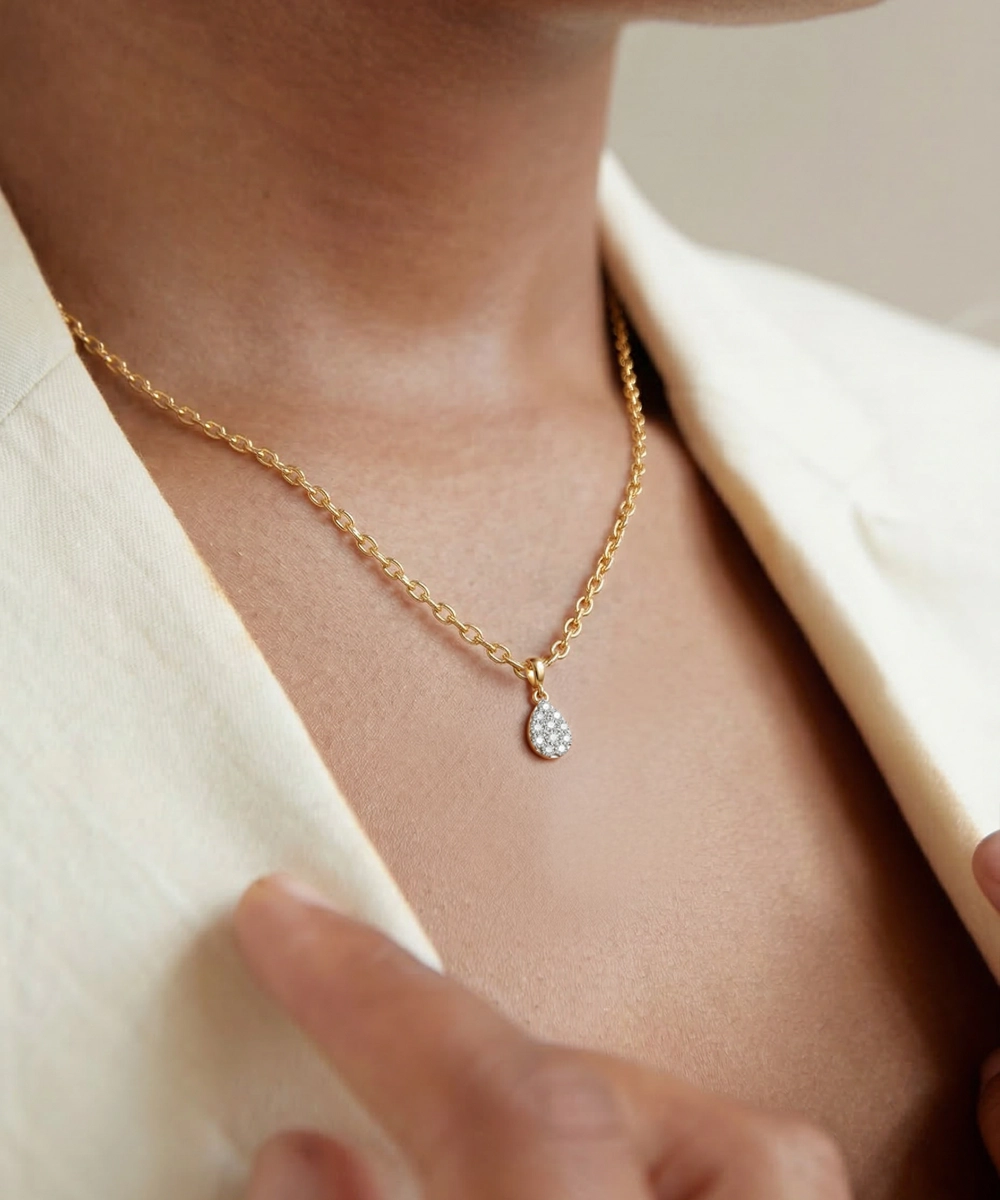 Gold necklace with a small pendant worn by a person in a beige outfit.