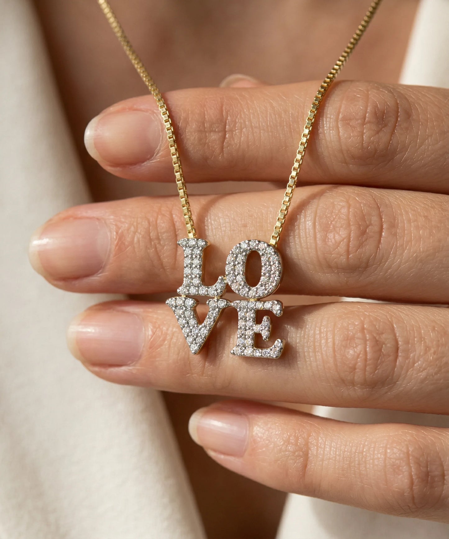 Gold necklace with 'LOVE' pendant held between fingers
