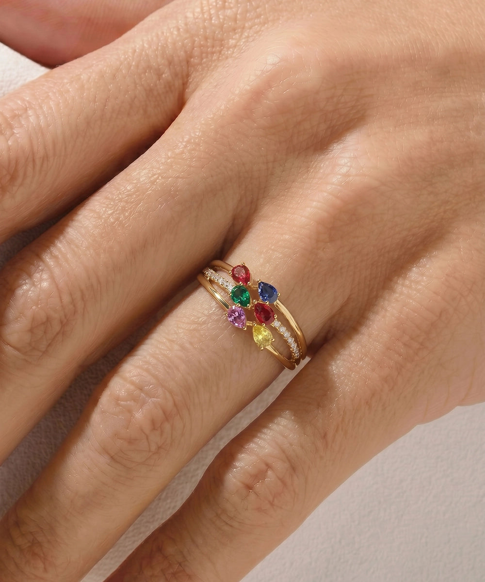 Close-up of a hand wearing a gold ring with multicolored gemstones on a neutral background