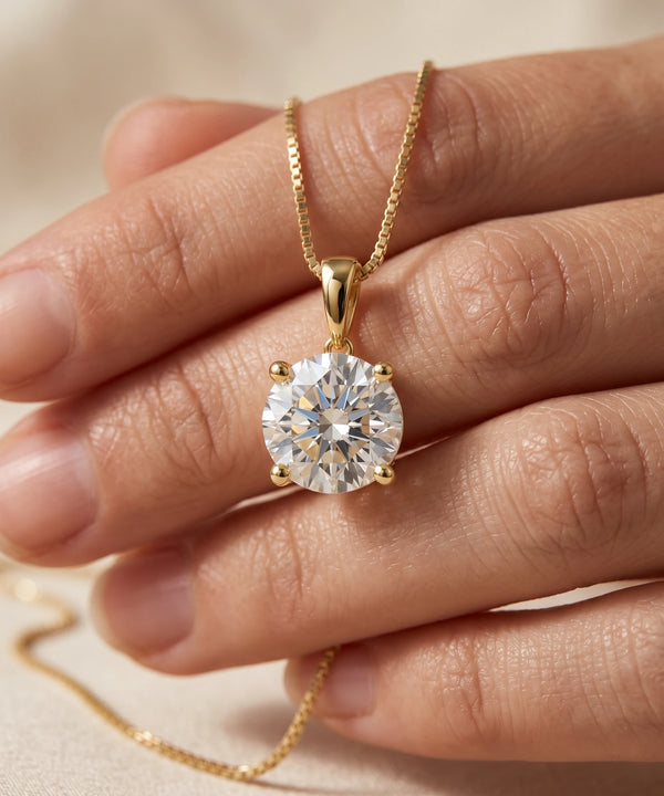Gold necklace with a diamond pendant held by a hand on a neutral background