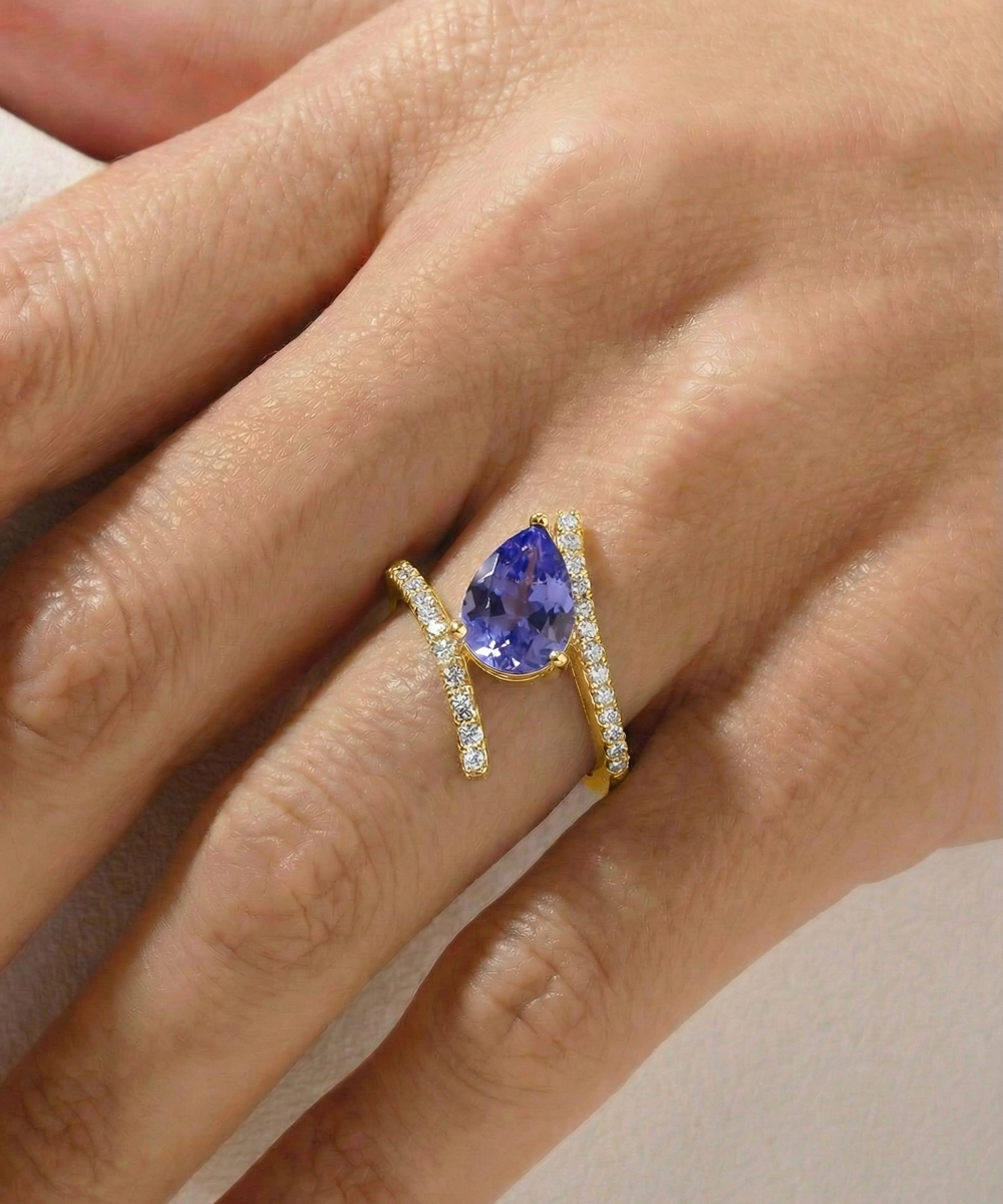 Gold ring with a blue gemstone on a hand against a neutral background