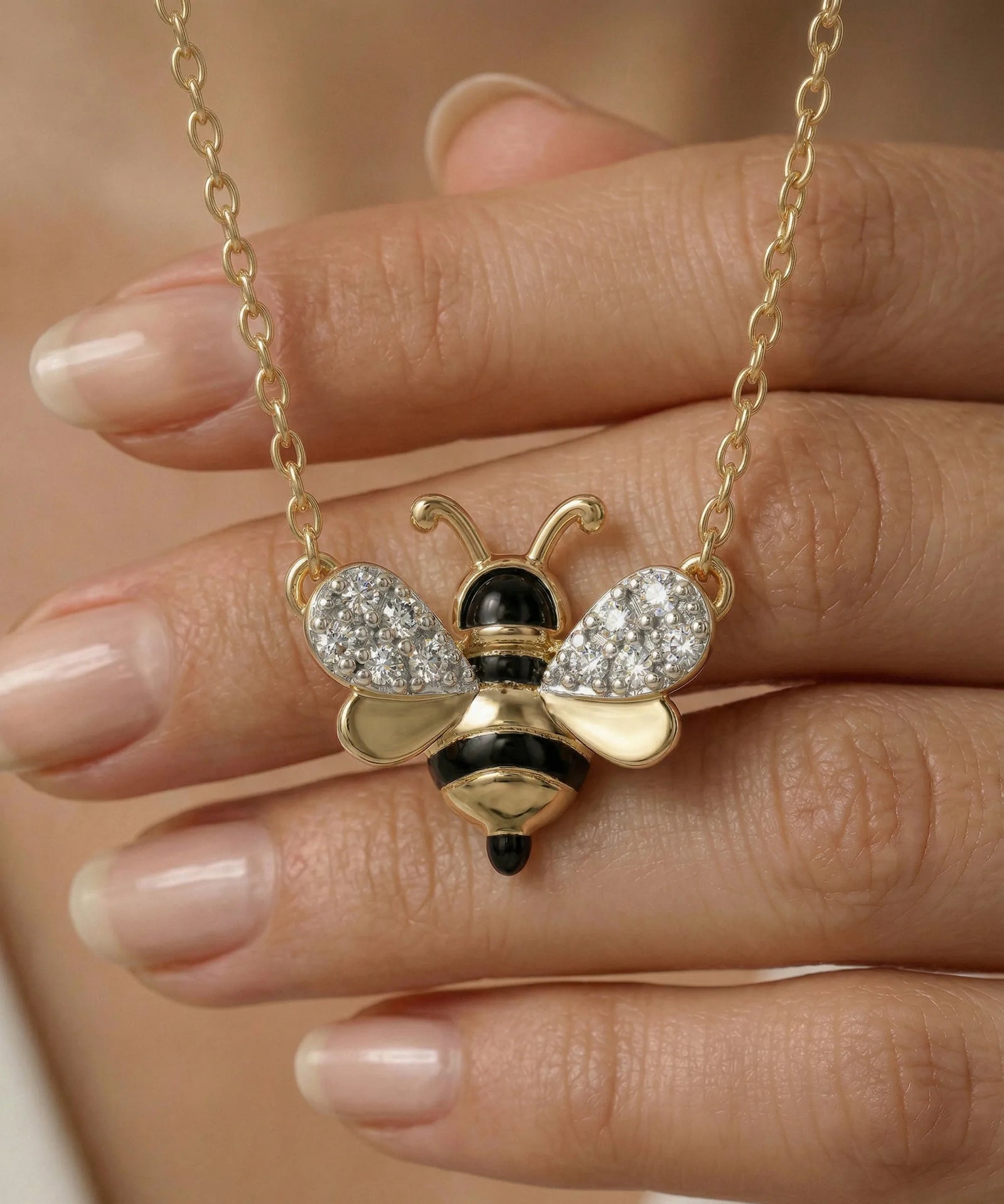 Gold bee-shaped necklace with black and white details held by a hand.