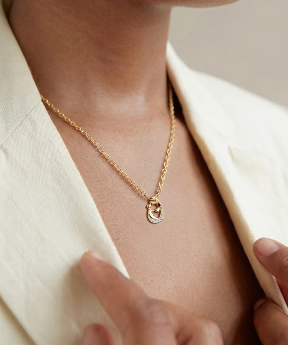 Gold necklace with a pendant worn by a person in a cream-colored outfit.