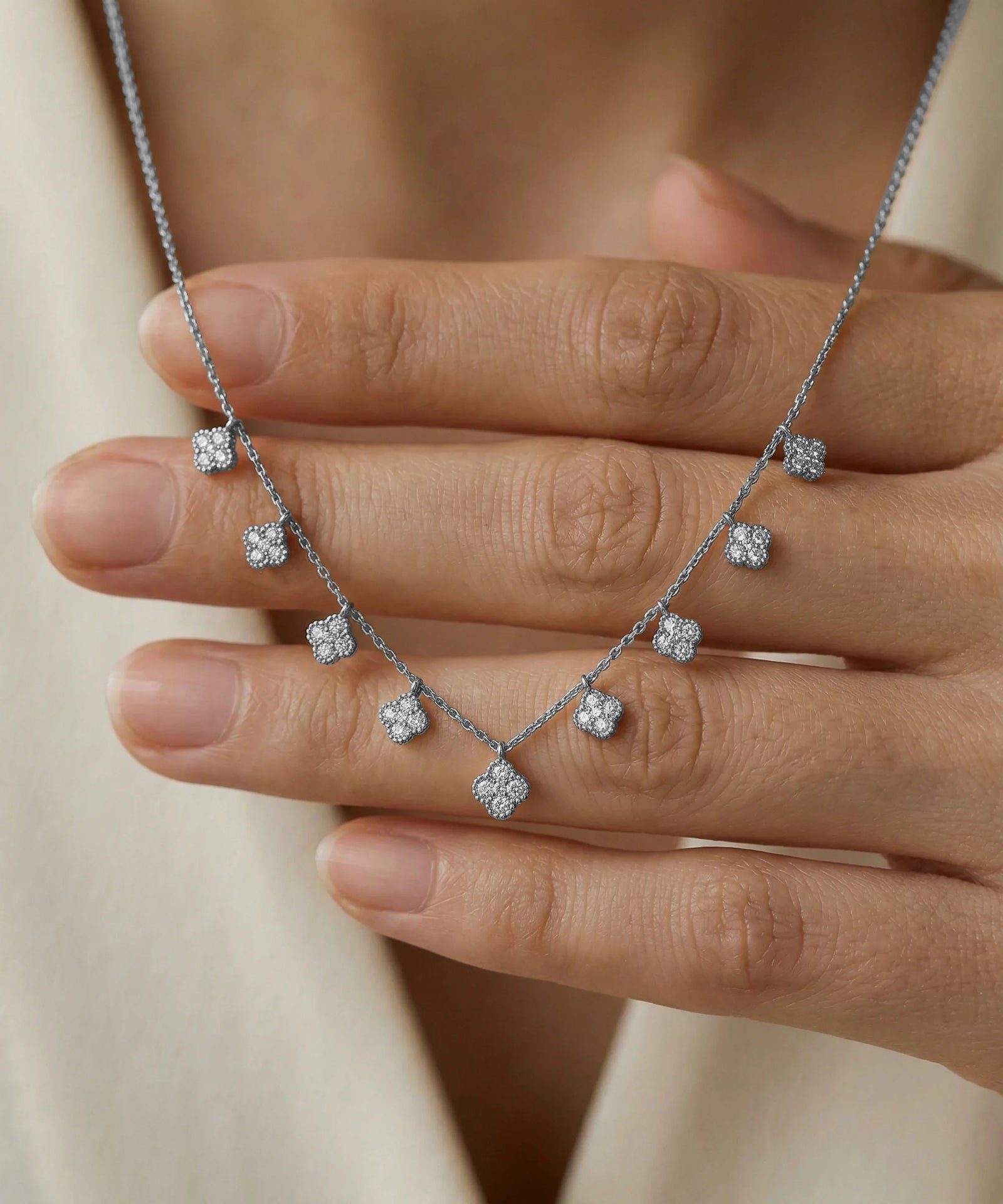 Silver necklace with diamond pendants held by a hand against a neutral background