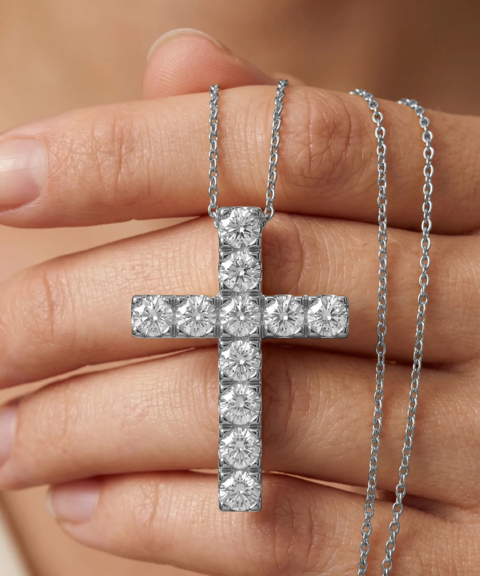 Silver cross necklace held between fingers against a neutral background