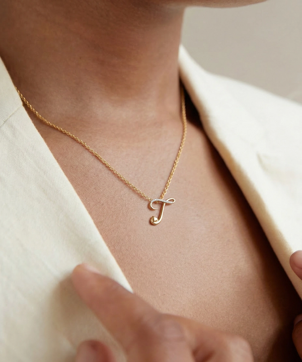 Gold necklace with a letter 'J' pendant on a person wearing a beige outfit.