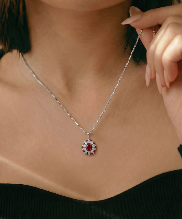 Close-up of a person wearing a silver necklace with a red gemstone pendant.