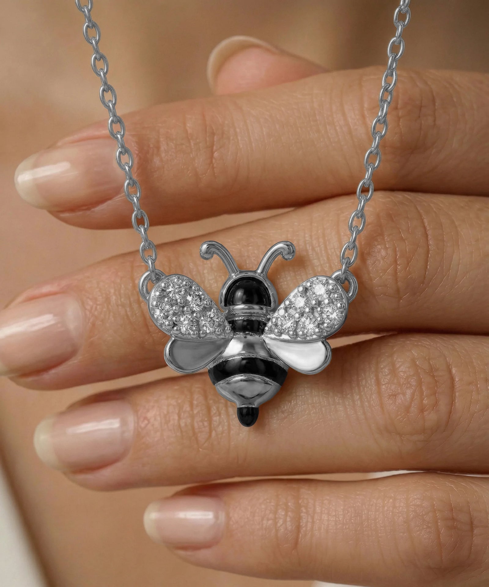 Silver bee-shaped pendant necklace held between fingers