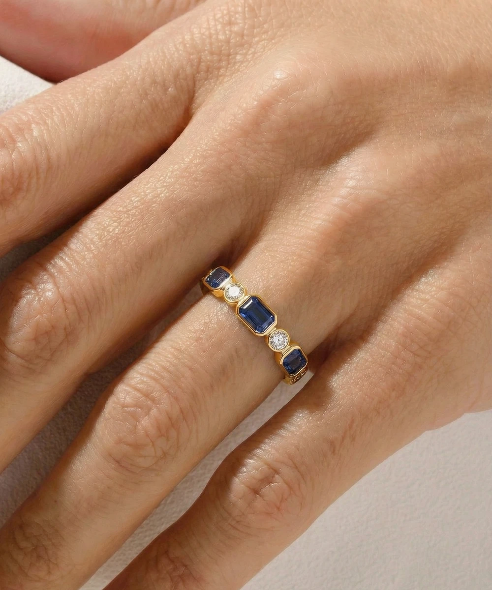 Gold ring with blue gemstones on a hand against a neutral background