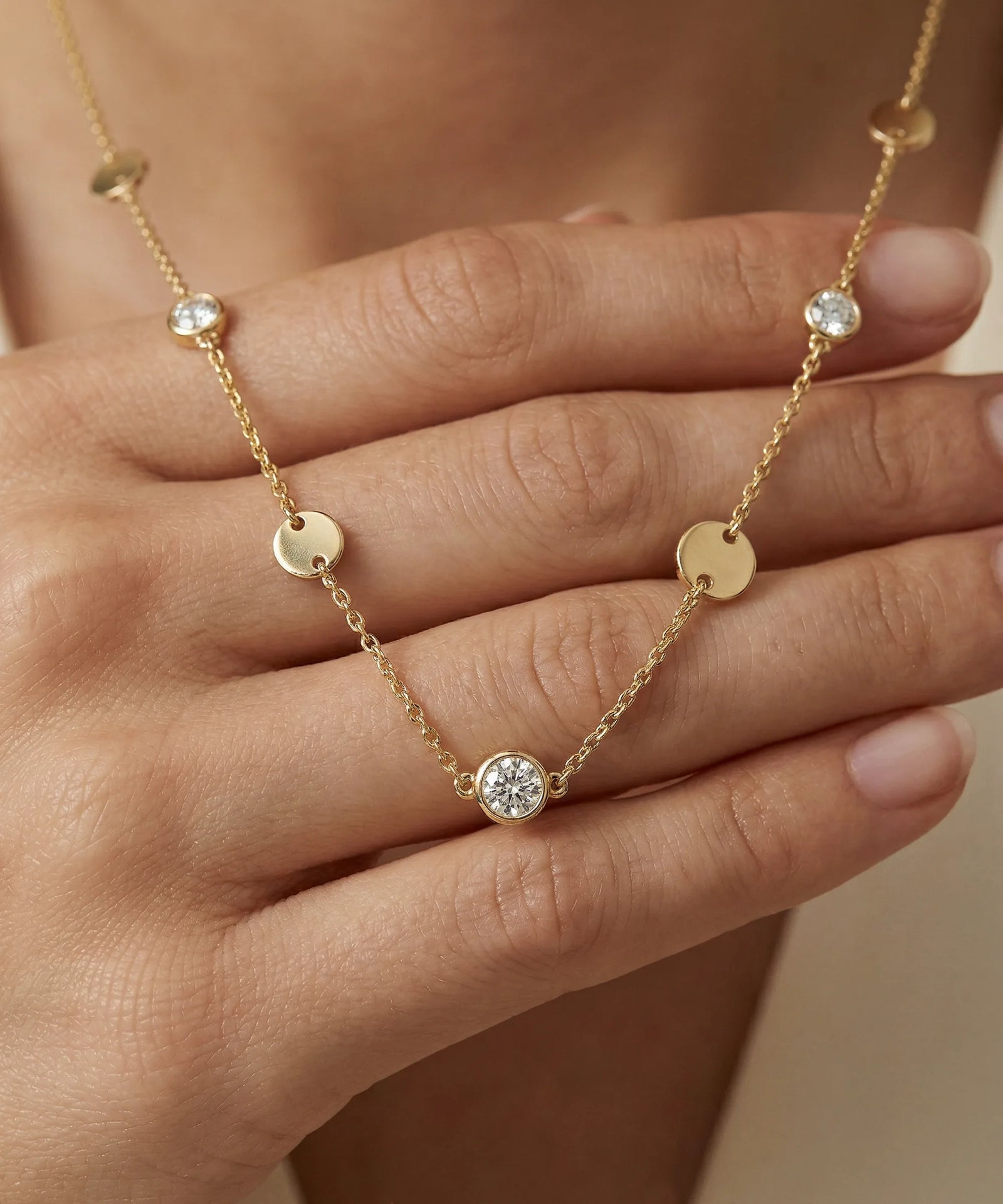 Gold necklace with small round pendants held by a hand against a neutral background