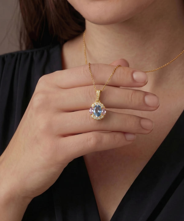 Gold necklace with a pendant featuring a blue gemstone held by a hand against a dark background