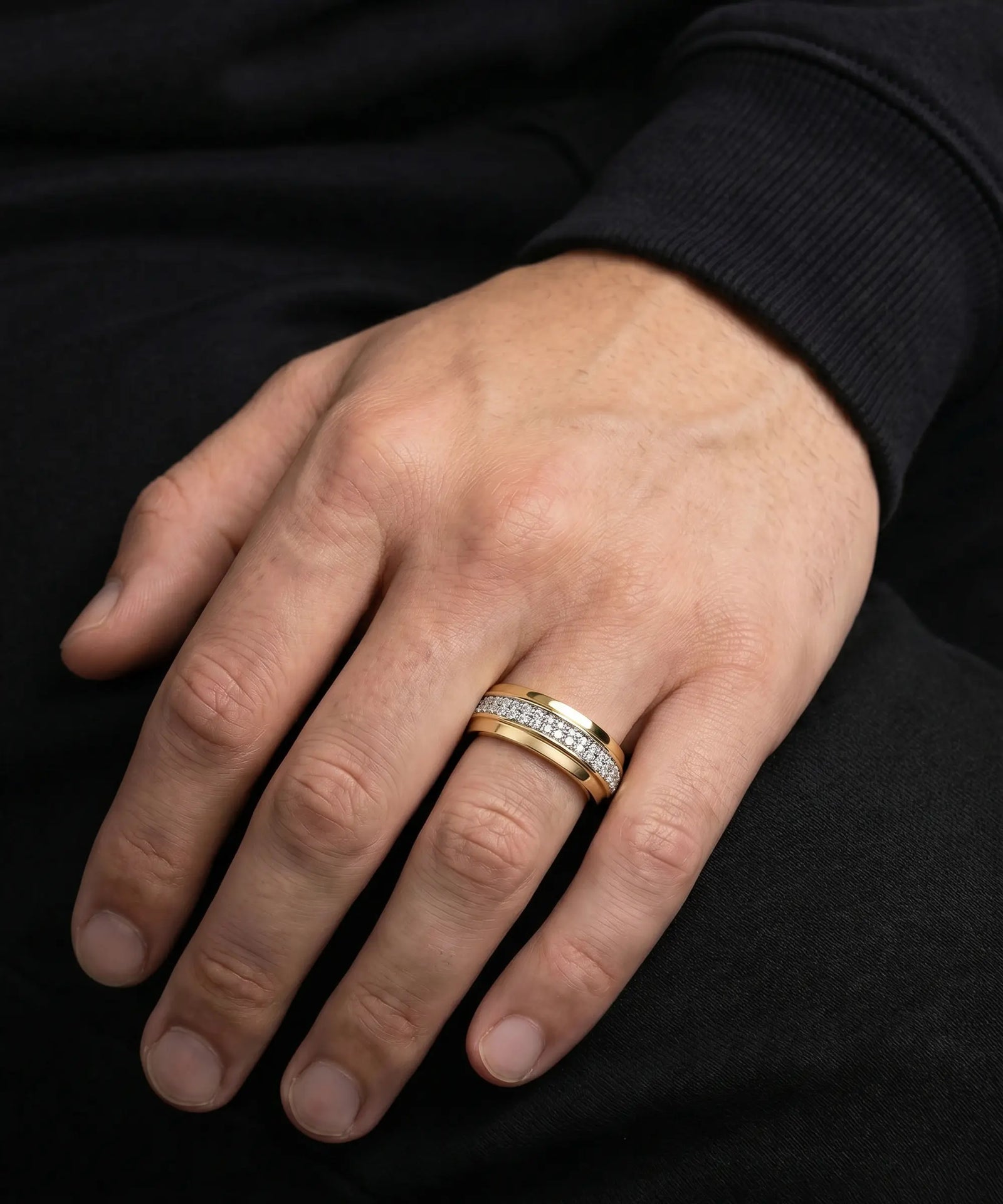 Hand wearing a gold ring with diamonds on a black background