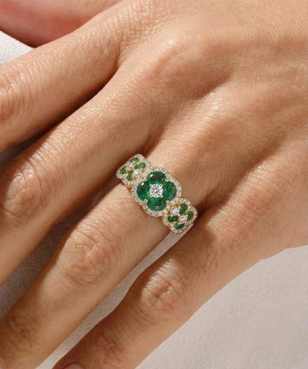 Gold ring with emeralds on a hand against a neutral background