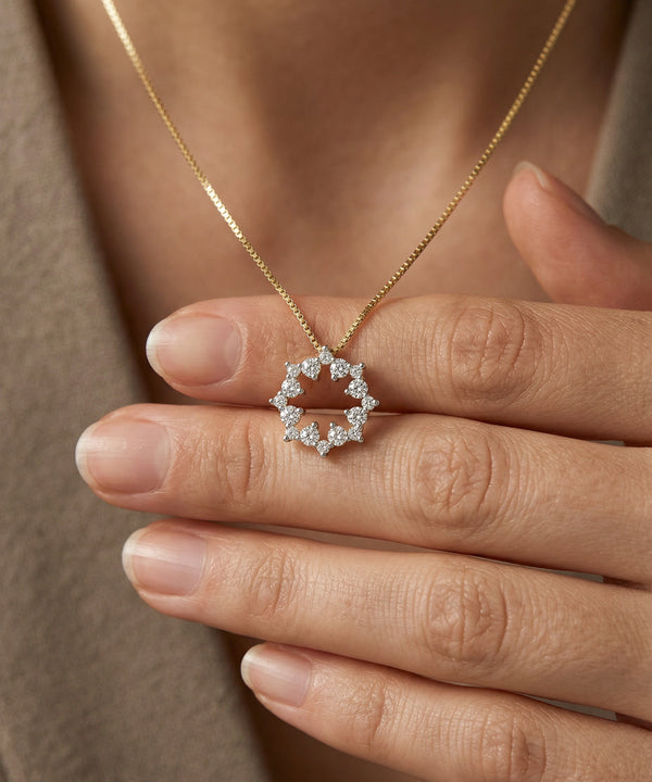 Gold necklace with a diamond pendant held by a hand against a neutral background