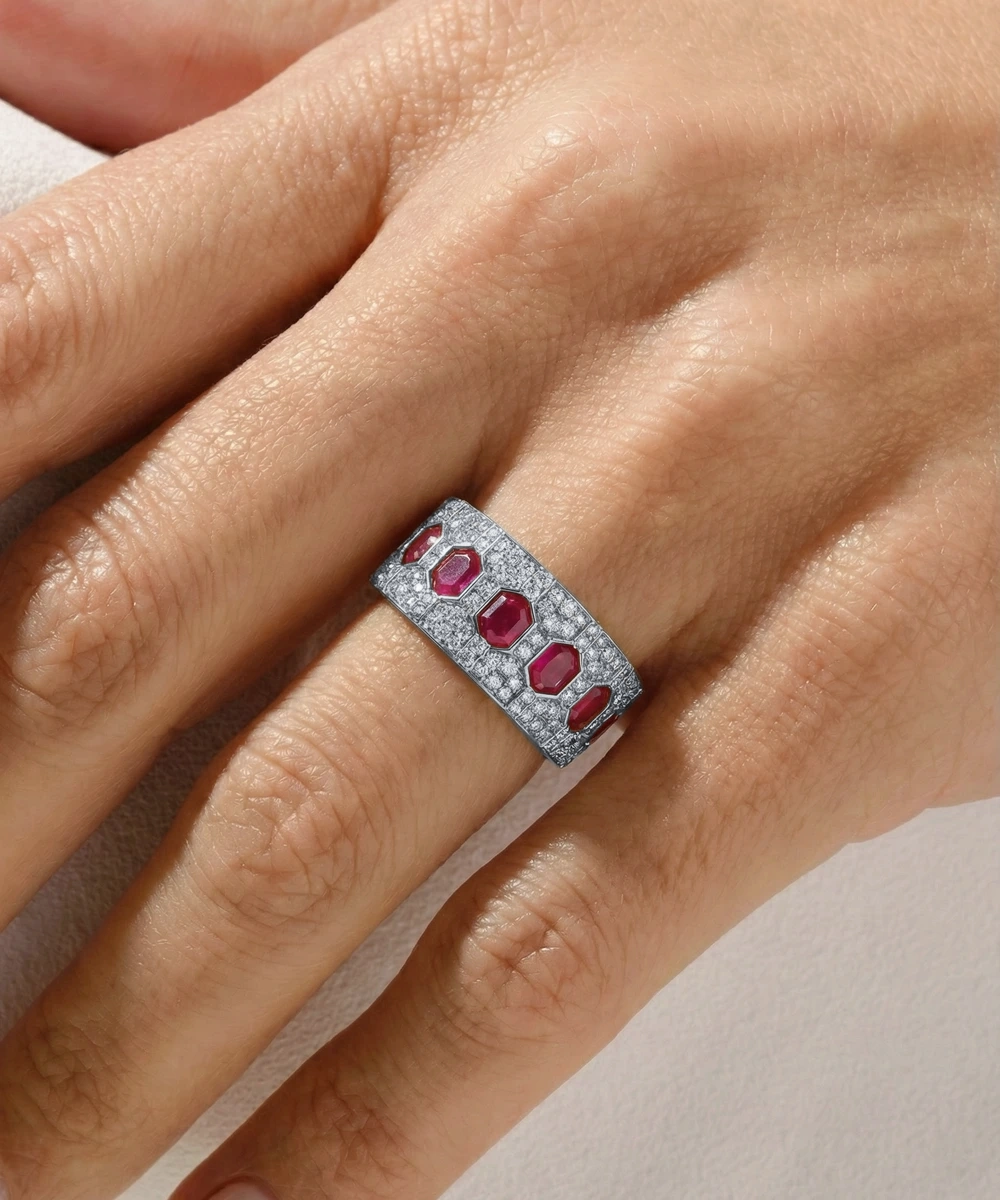 Silver ring with red gemstones on a hand against a neutral background