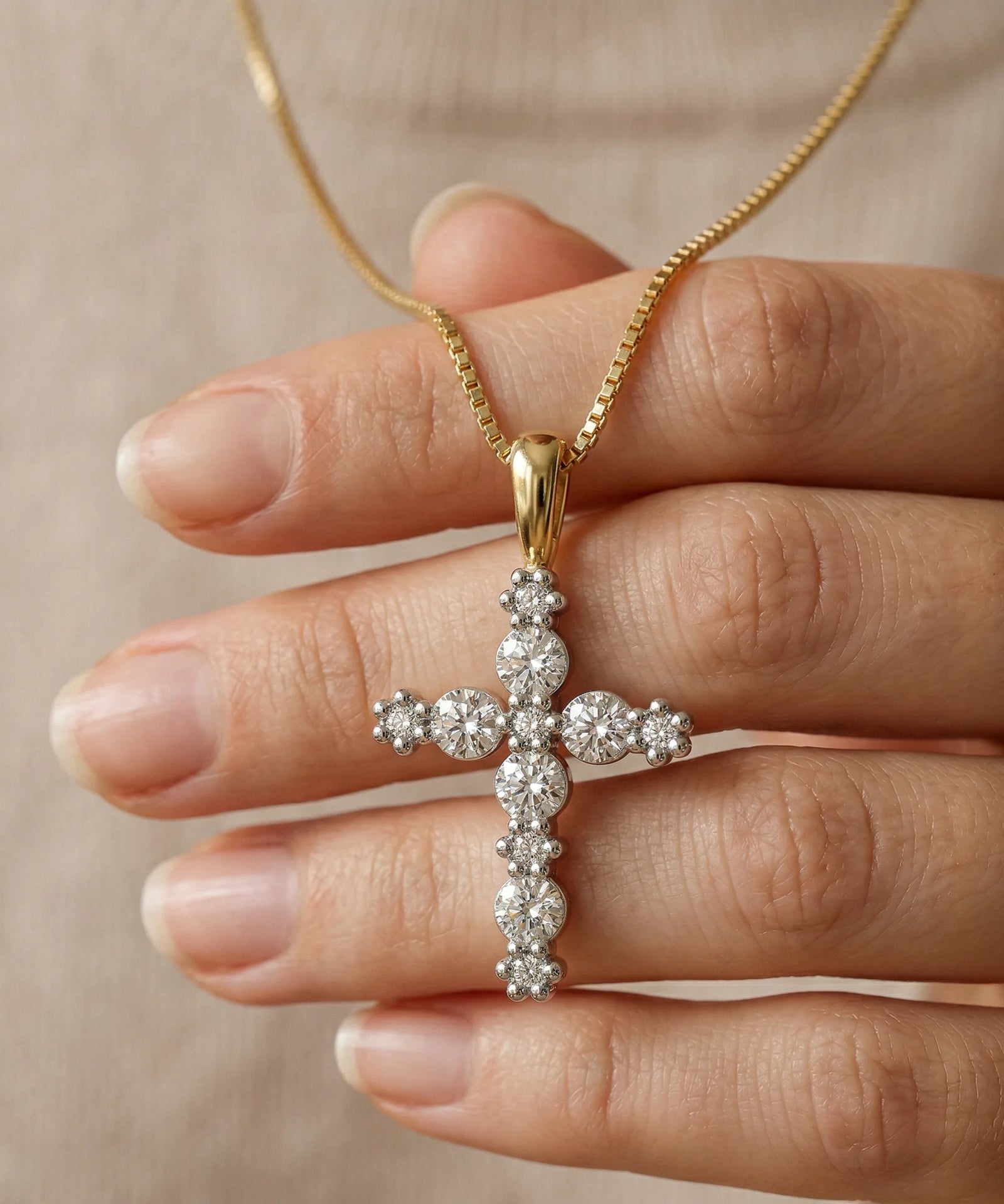 Gold necklace with a diamond cross pendant held by a hand against a beige background