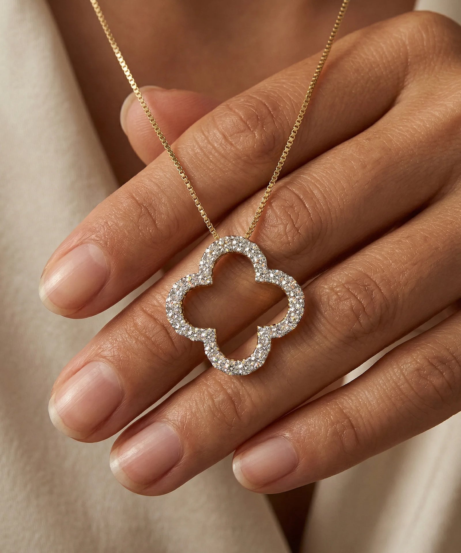 Silver quatrefoil pendant on a gold chain held by a hand against a neutral background