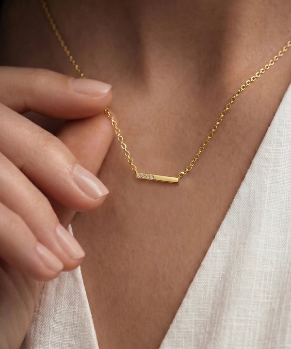 Gold necklace with a bar pendant on a person wearing a white top.