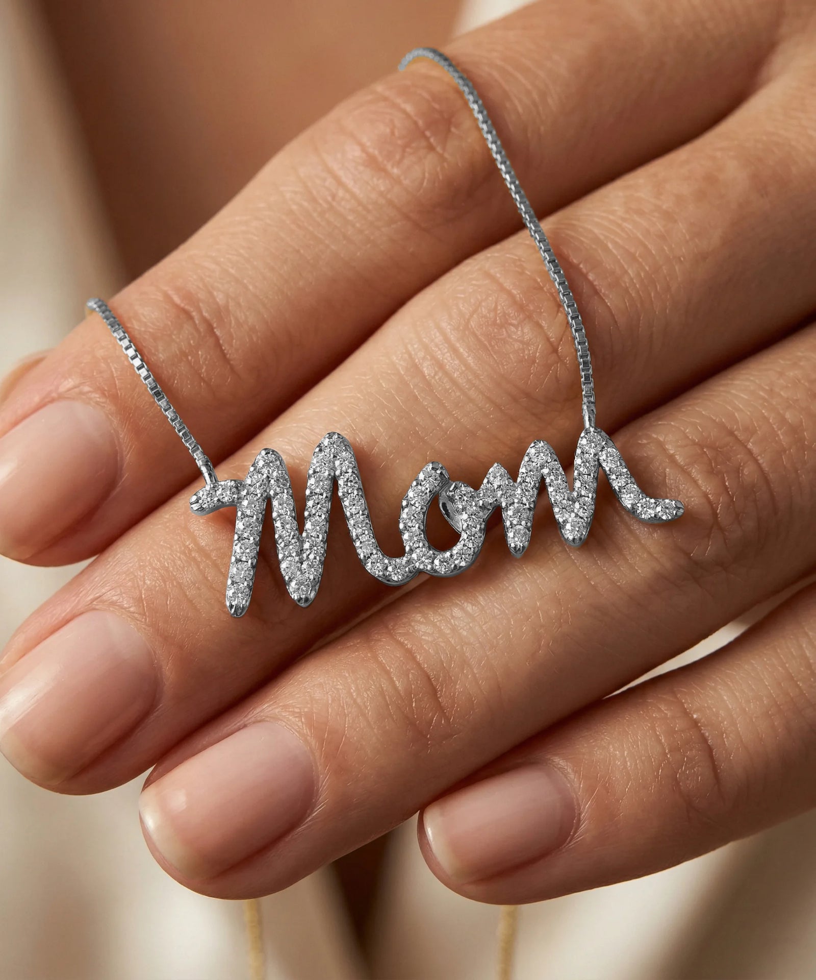 Silver 'Mom' necklace on a hand against a neutral background