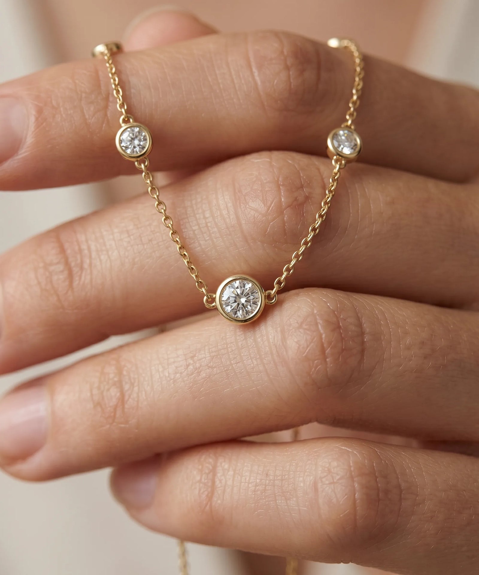 Gold necklace with diamond pendants on a hand against a neutral background