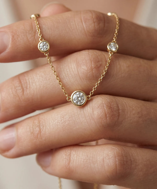 Gold necklace with diamond pendants on a hand against a neutral background