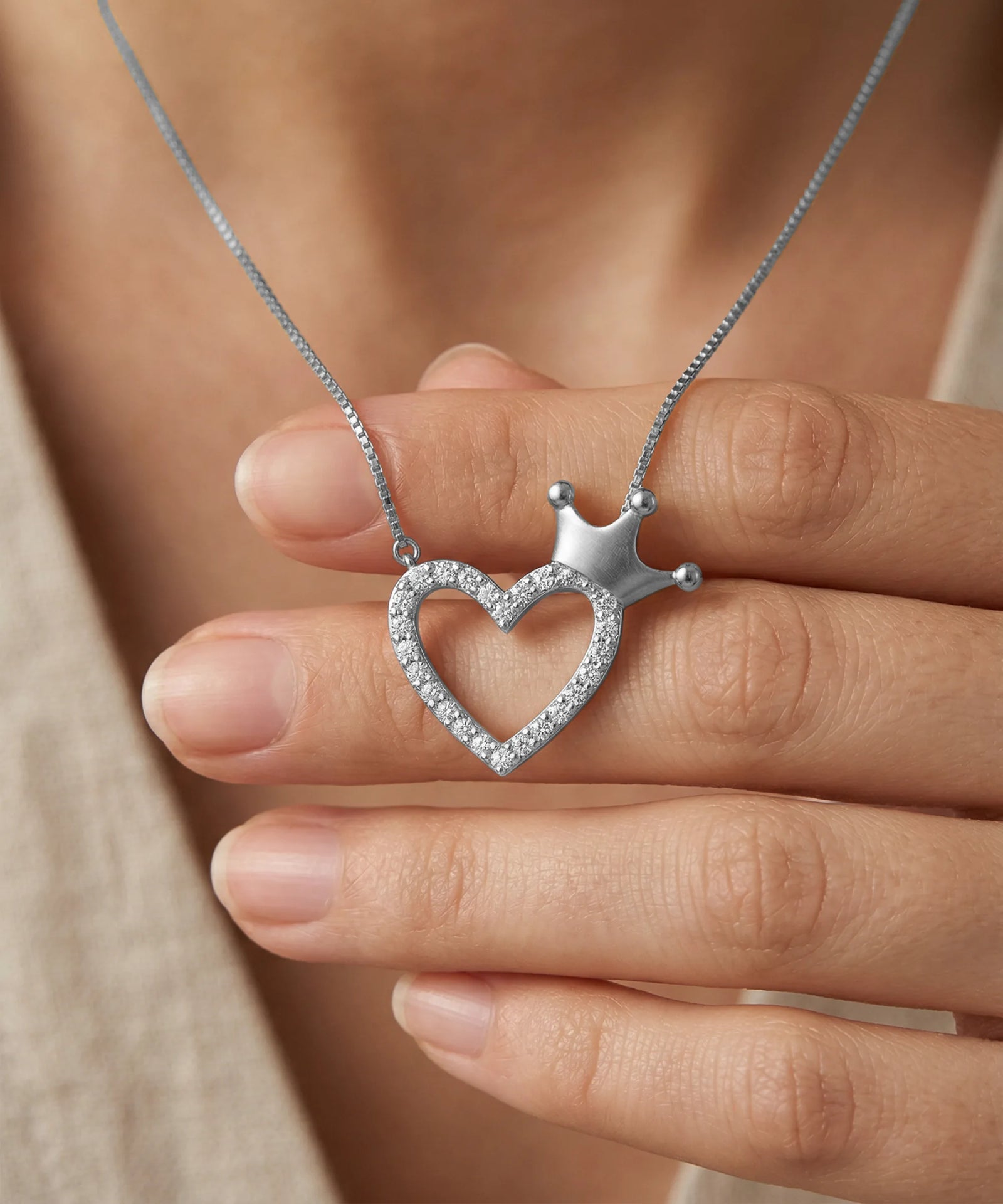 Heart-shaped pendant with a crown on a chain held by a hand