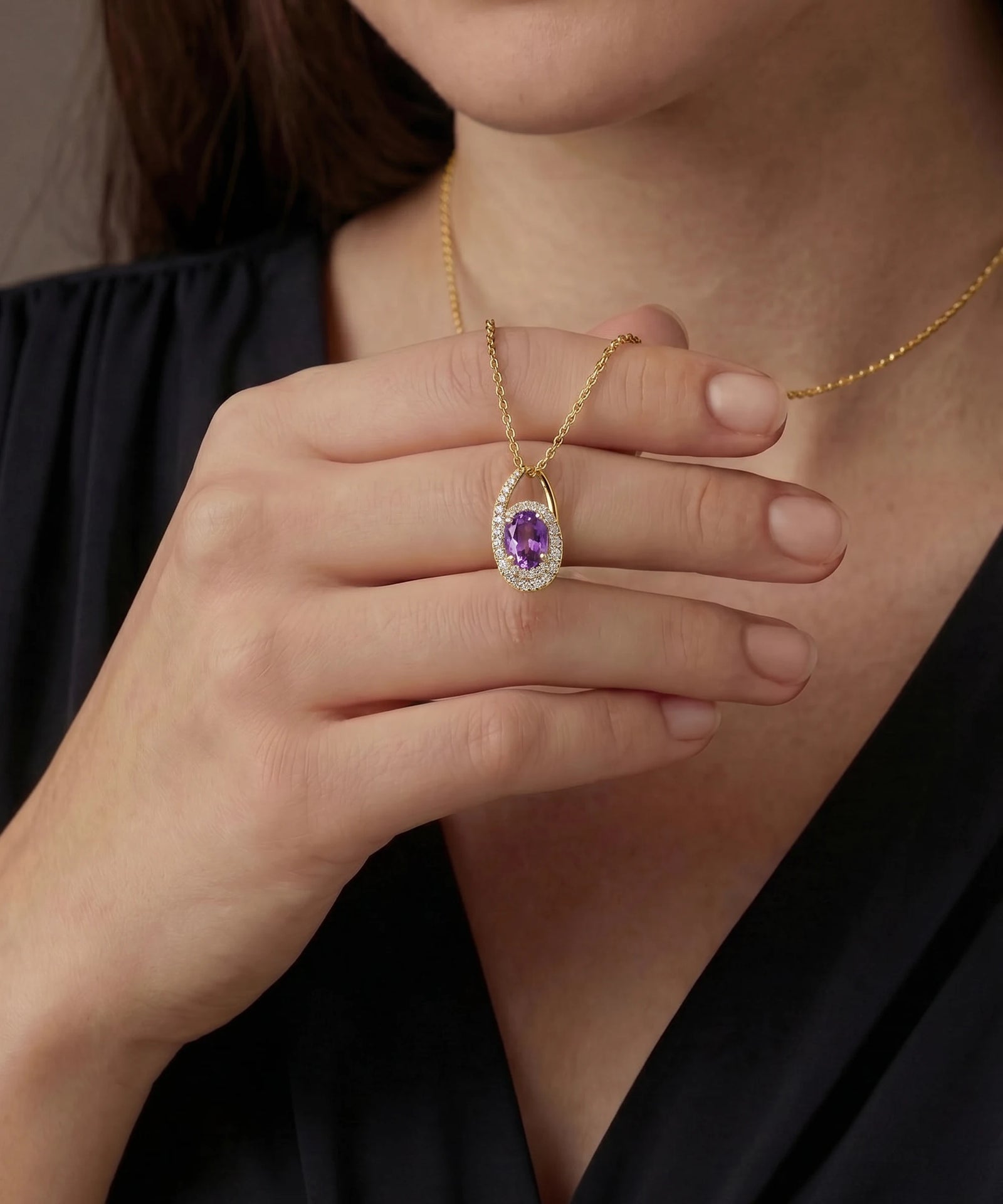 Gold necklace with a purple gemstone held by a hand against a neutral background