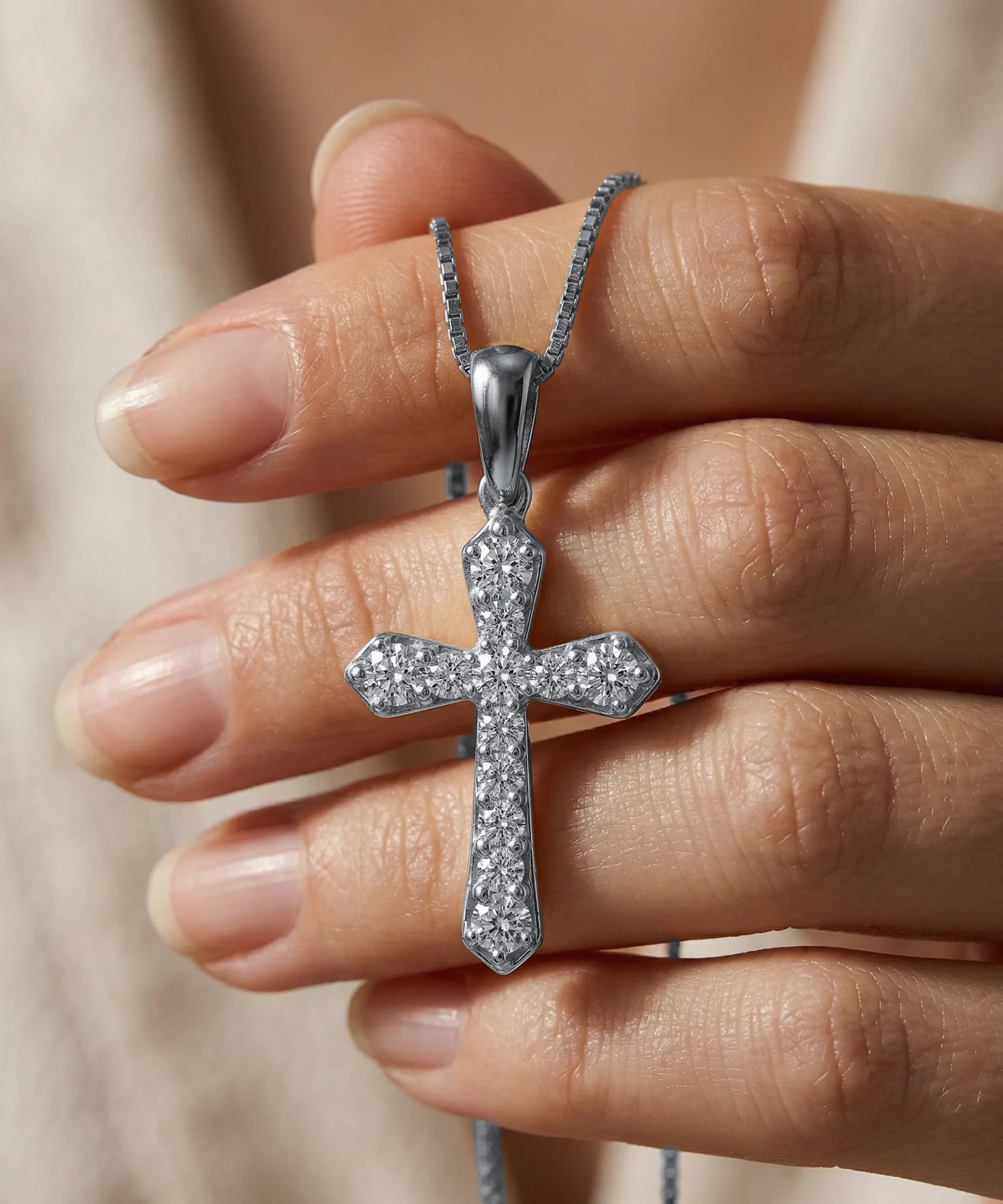 Silver cross pendant necklace held in a hand against a neutral background