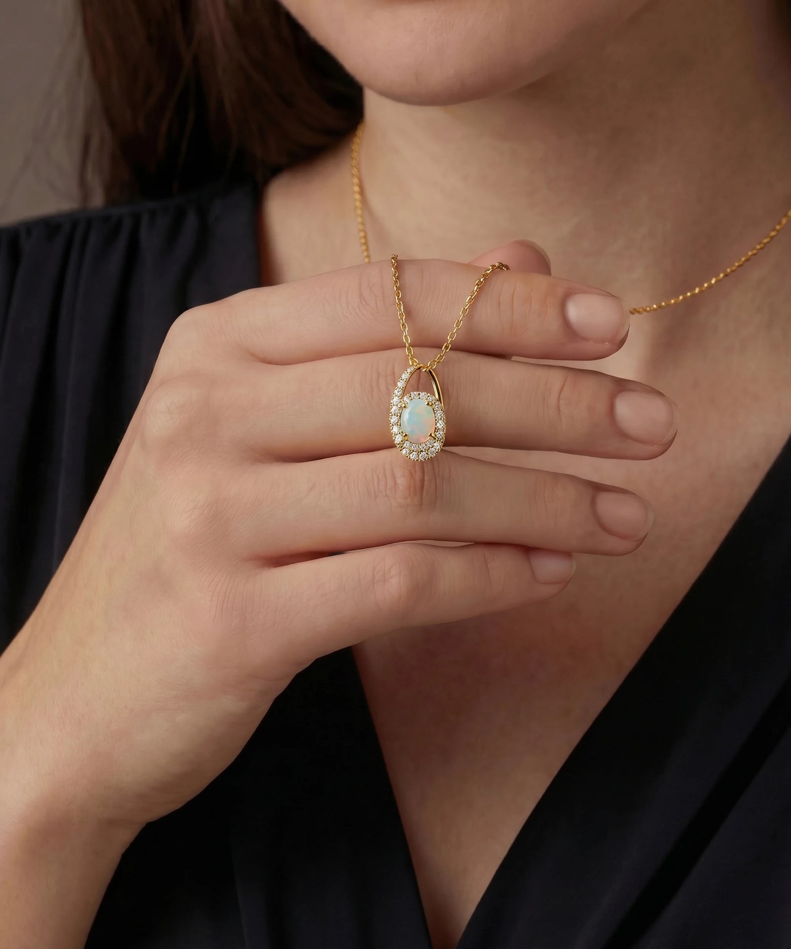 Gold necklace with a pendant held by a hand against a neutral background