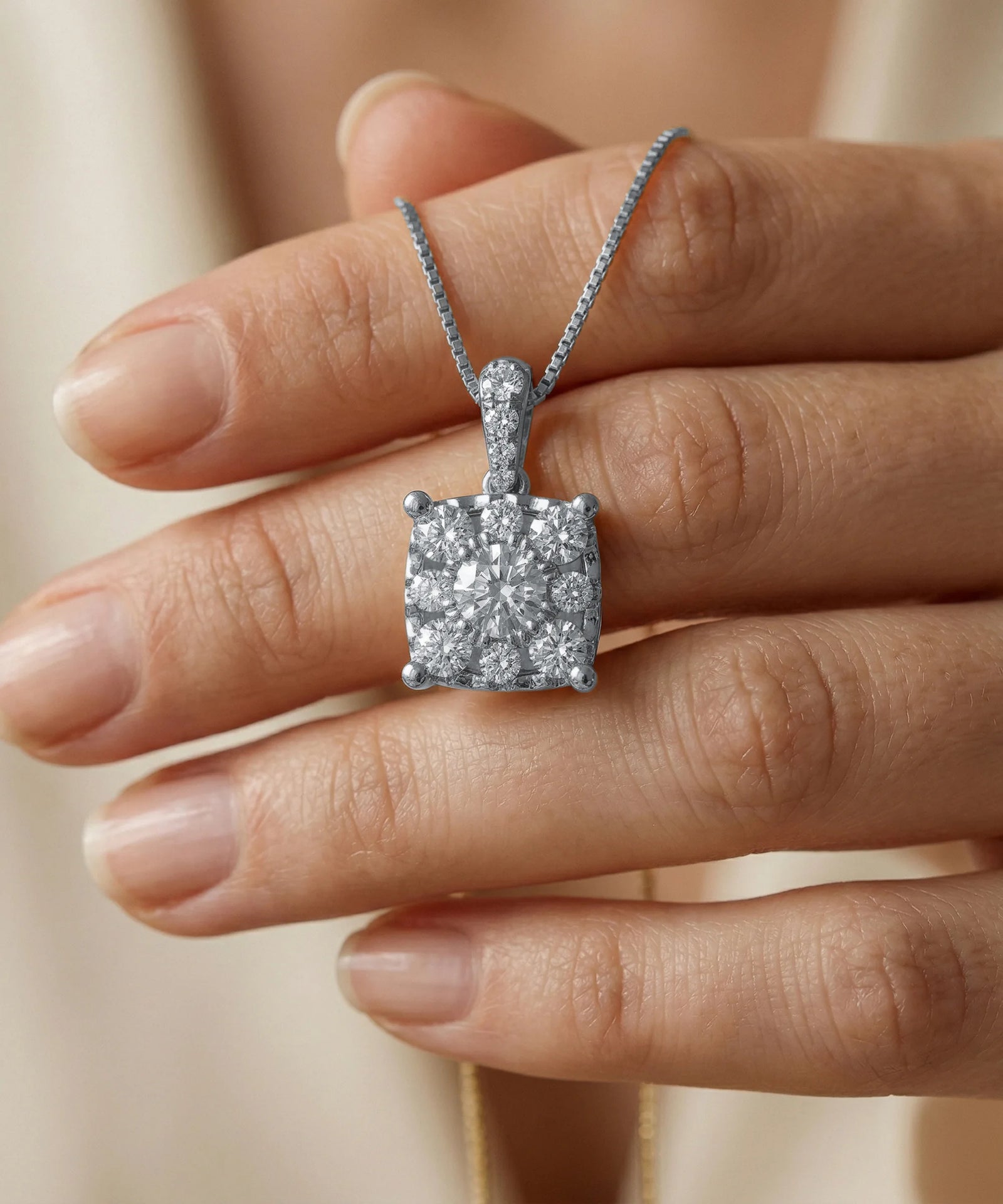 Diamond necklace held between fingers against a neutral background