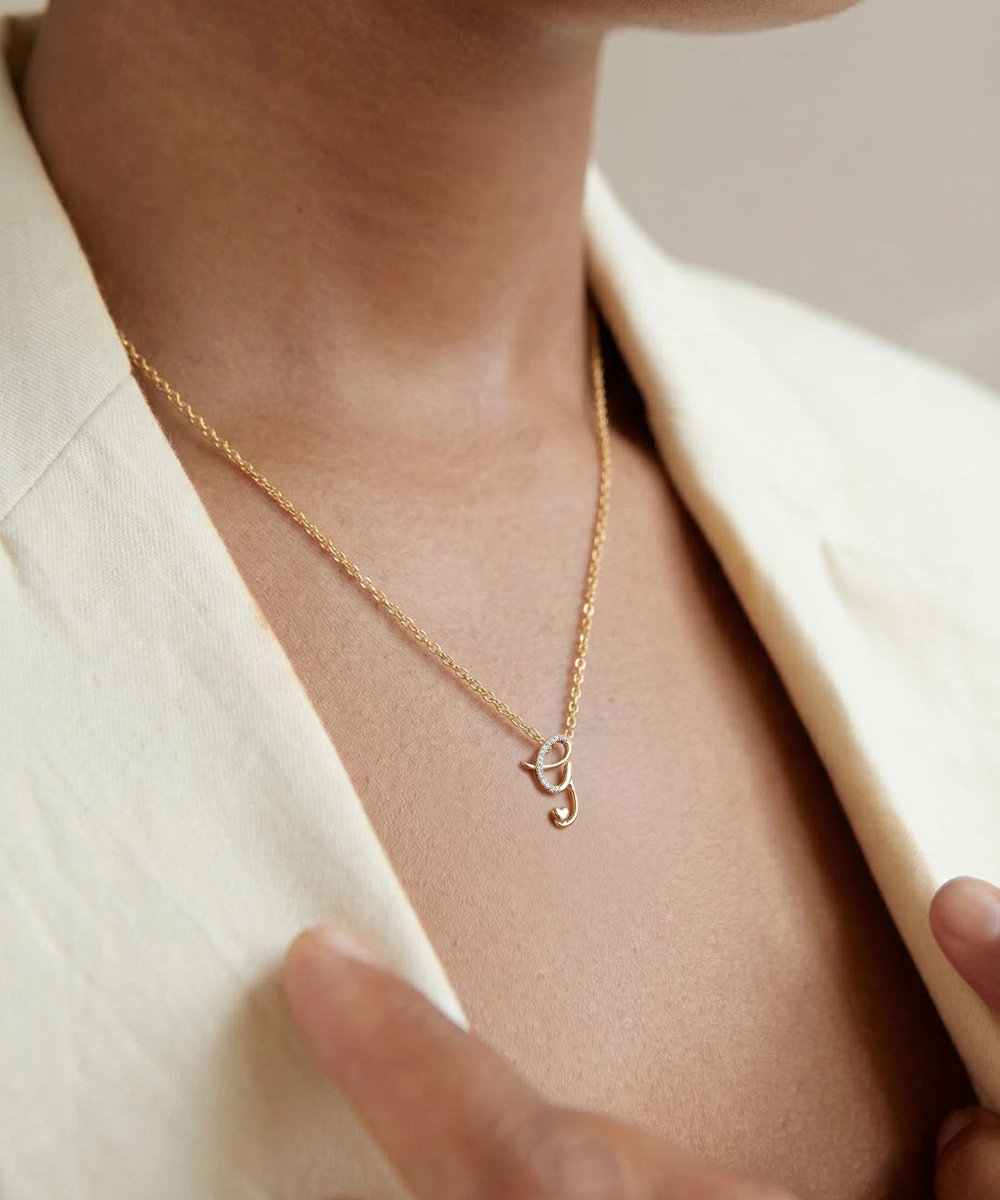 Gold necklace with a small pendant worn by a person in a cream blazer.