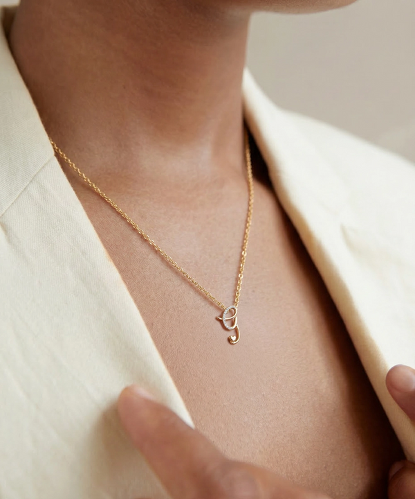 Gold necklace with a small pendant worn by a person in a cream blazer.
