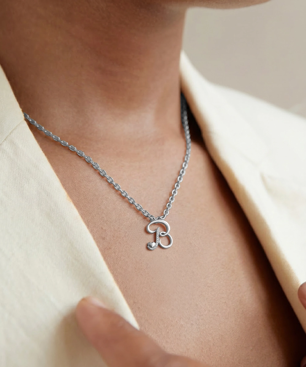 Silver necklace with a unique pendant on a person wearing a beige outfit.