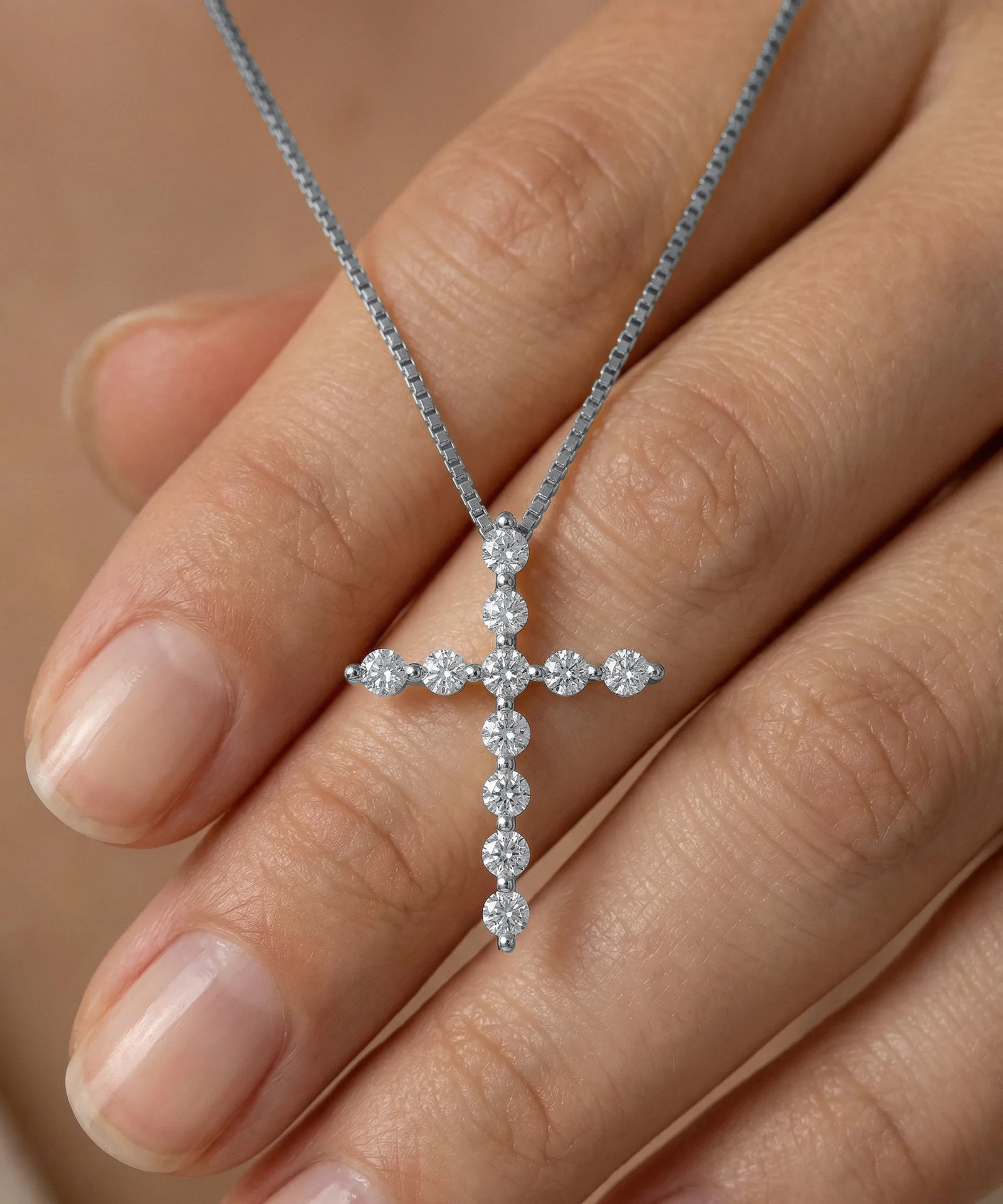 Diamond cross necklace held by a hand against a neutral background