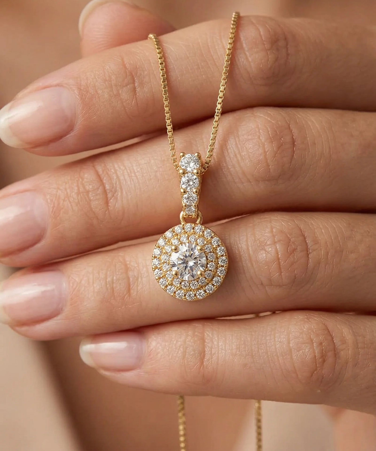 Gold necklace with a diamond pendant held by a hand