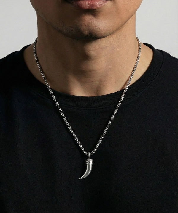 Person wearing a black shirt with a silver necklace featuring a horn pendant against a neutral background