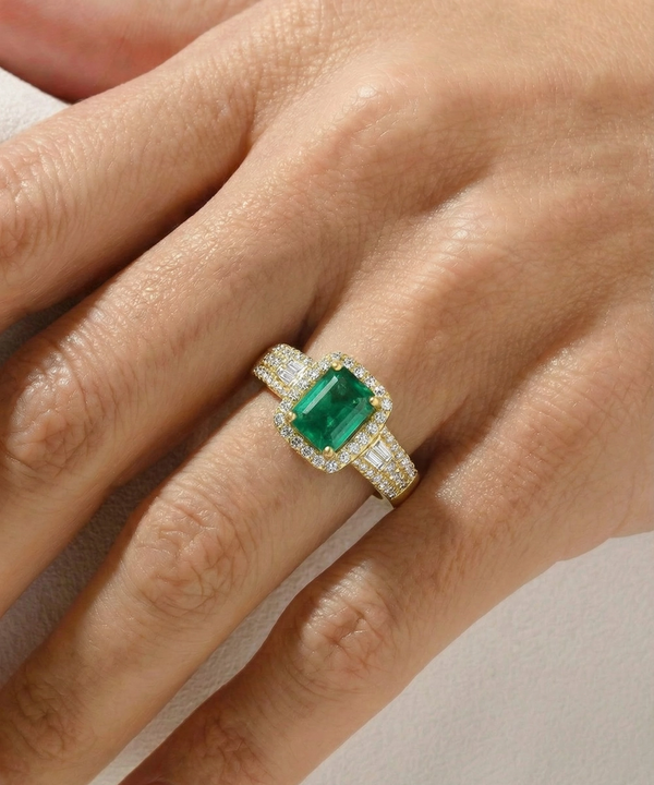 Gold ring with a green gemstone on a hand against a neutral background