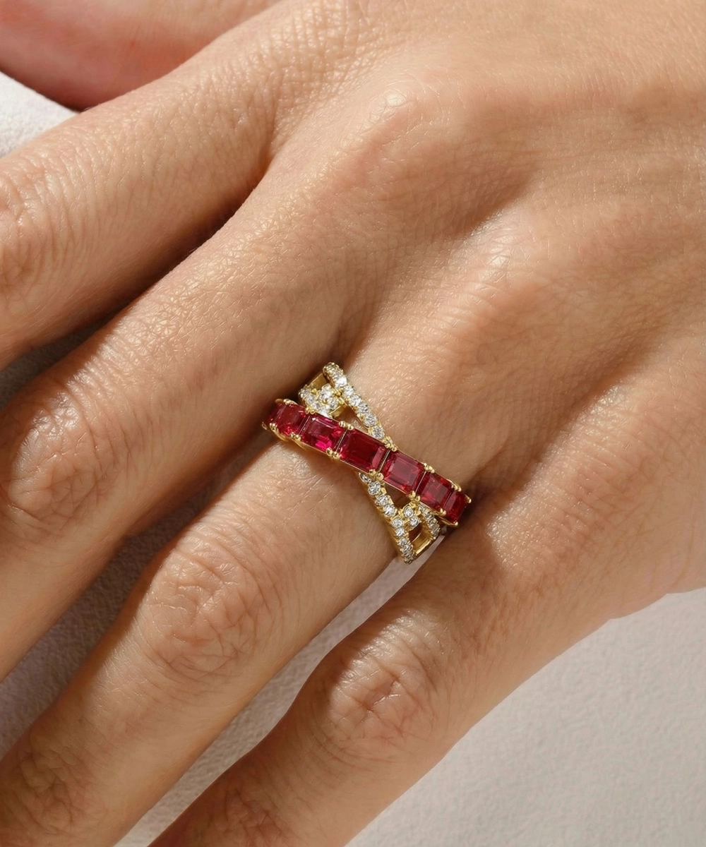 Gold ring with red gemstones on a hand against a neutral background
