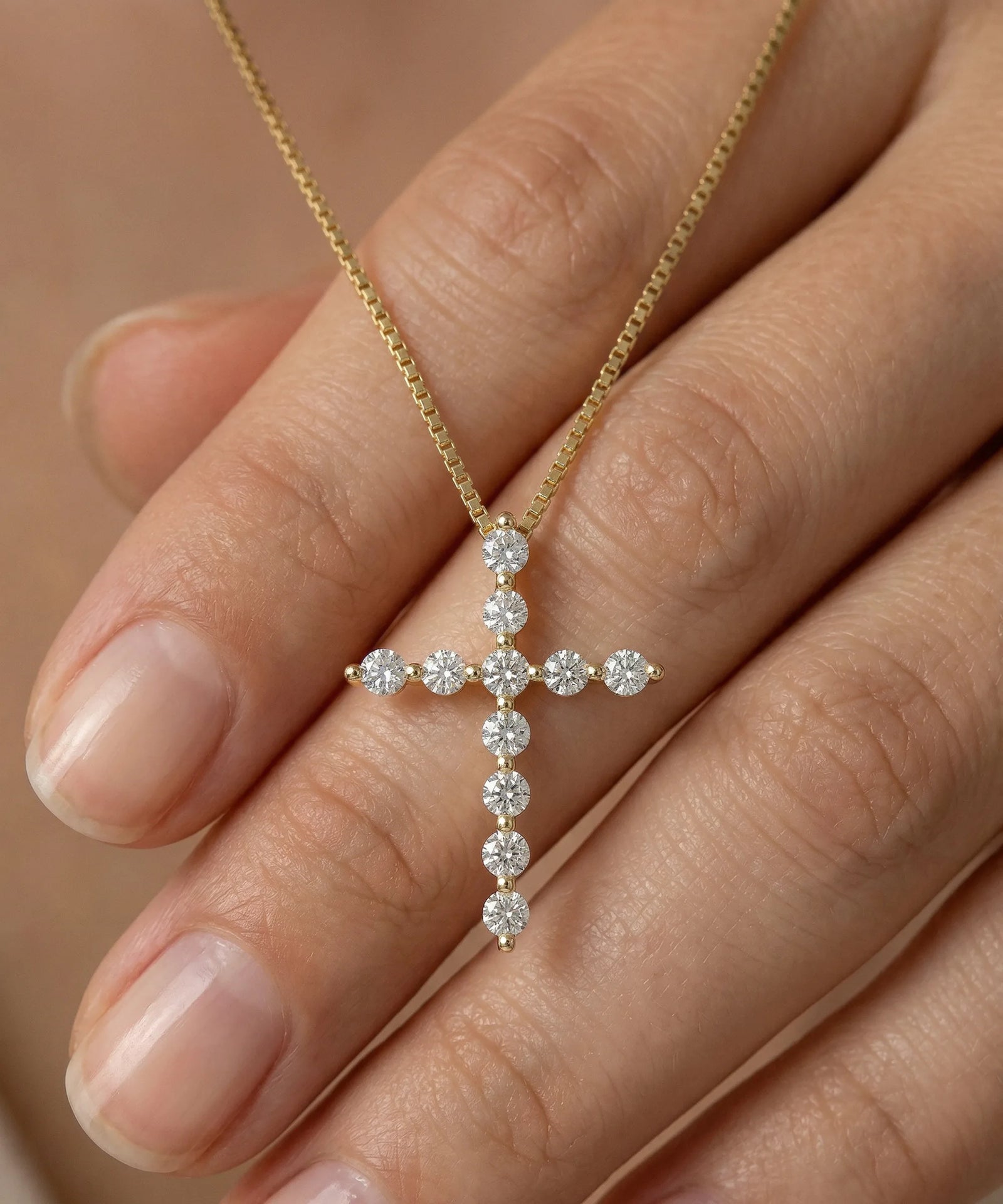 Gold cross necklace with diamonds held between fingers against a neutral background