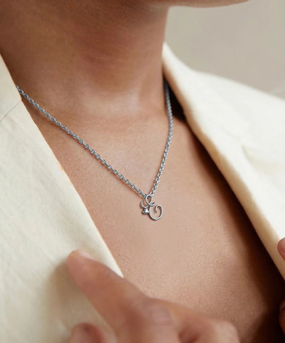 Silver necklace with a pendant worn by a person in a light-colored outfit.